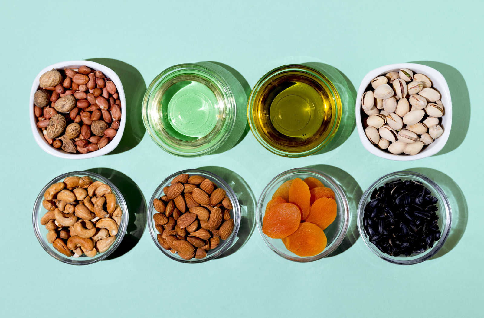 A set of natural foods, including nuts and seeds, that are rich in vitamin E. The products are arranged on a teal background.