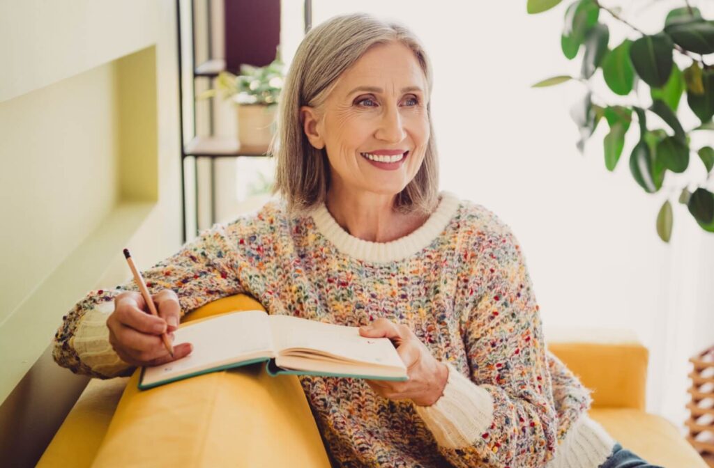 An older adult smiling on their couch while thinking of what to write in their new journal.