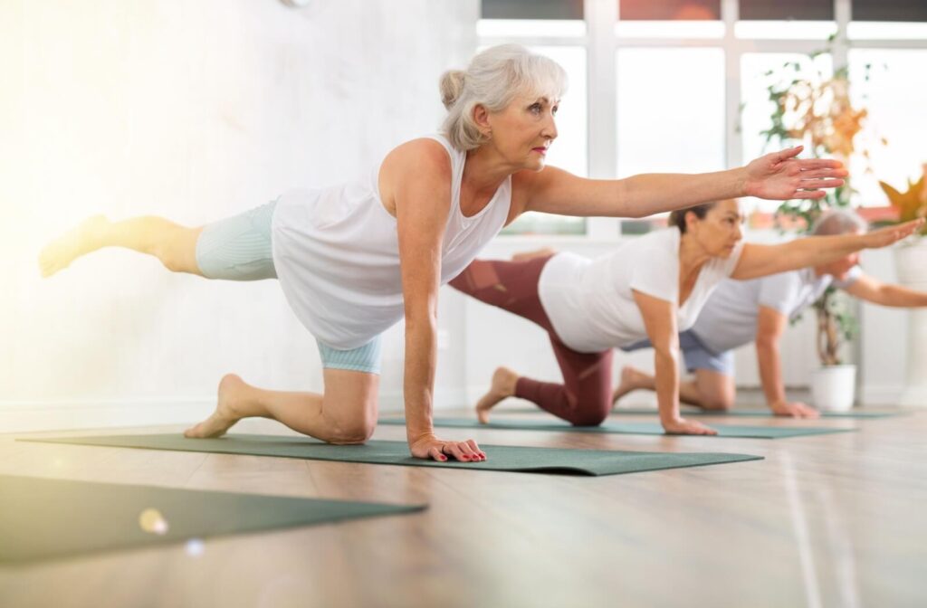 A group of older adults stretching in the bird-dog yoga pose in a fitness class to improve their posture.